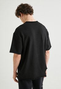 Schwarzes, übergroßes T-Shirt mit einem rohen Saum, kurzen Ärmeln und ohne sichtbare Nähte am Kragen. Weicher Stoff mit einer lockeren Passform.