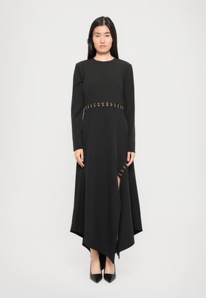 Black long-sleeve dress with asymmetric hem, featuring gold accents at the waist and side slit. Smooth fabric texture.