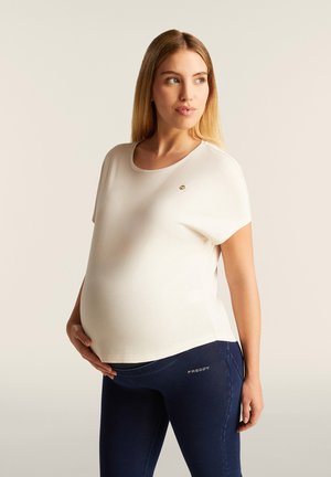 Top de maternidad de color crema con mangas cortas y escote redondeado, combinado con leggins elásticos de color azul oscuro que presentan un logo en la cinturilla.