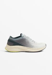 Basket de course légère avec une tige en mesh gris clair et des accents vert foncé, une semelle crème rembourrée et un design texturé.