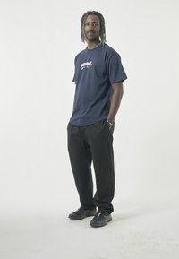 Navy blue cotton t-shirt with short sleeves and graphic print. Paired with black pants and black athletic shoes. Simple, casual design.