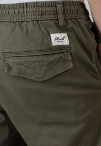 Olijf groene katoenen shorts met elastische tailleband, voorzien van een achterzak met flap en een wit label dat in de tailleband is gestikt.
