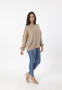 Beige gebreid sweater met een drop shoulder, gecombineerd met blauwe skinny jeans en transparante hak-sandalen. Zachte textuur en een ontspannen pasvorm.