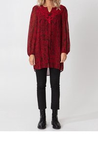 Blouse rouge transparente avec un motif floral et un col texturé, associée à un pantalon noir ajusté et des bottines noires. Manches longues bouffantes.