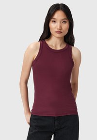 Top ajustado burdeos con textura acanalada, cuello redondo y tirantes anchos, combinado con pantalones de mezclilla oscuros.