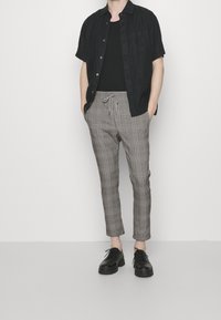 Korte mouwen zwarte shirt, zwarte tanktop en grijs geruite broek met elastische tailleband. Zwarte veterschoenen maken de outfit compleet.