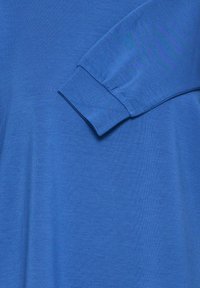 Chemise bleue à texture lisse, dotée d'un col arrondi et de manches longues avec des poignets détaillés. Design simple et monochrome.