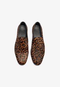 Zapatillas de lona con estampado de leopardo en una combinación de colores marrón y negro, con una parte superior de textura suave y un forro interior negro.