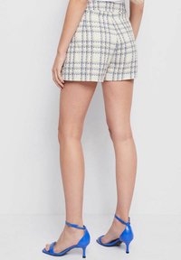 Lichtgekleurde tweed shorts met een blauw ruitpatroon, hoge taille en een gestructureerde afwerking; gecombineerd met blauwe hoge hakken.