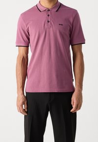 Rosa polo-shirt med svart krage, tre knappslå och liten logotyp. Tillverkad av mjukt tyg och har en klassisk passform.