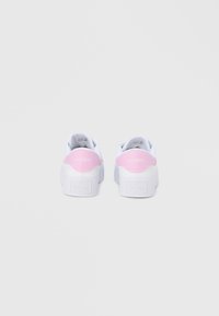 Λευκά αθλητικά παπούτσια με ροζ λεπτομέρεια στη φτέρνα, υφή υλικού και λογότυπο στο πίσω μέρος. Διαθέτουν απλό σχέδιο με κορδόνια και επίπεδη σόλα.