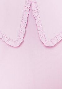 Měkká růžová látka s volánovým límcem, který má na okrajích nařasené detaily a trojúhelníkový výstřih ve středu.