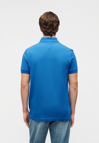 Polo à manches courtes en tissu bleu vif. Il présente un col classique et un dos fendu. Associé à un jean bleu clair.