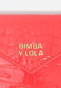 Czerwona lakierowana torebka ze skóry o fakturze krokodyla, z złotym logo "Bimba Y Lola" i trójkątnym klapą.