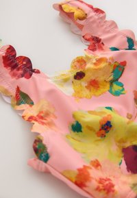 Lyserød blomsterbadedragt med en bølget halsudskæring, levende gule og røde blomsterprint og en glat stoftekstur.