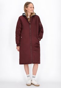 Abrigo largo burdeos con cremallera, capucha gris y bolsillos laterales. Textura suave con hardware metálico notable y puños elásticos.