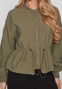 Bomberka w oliwkowym kolorze z zamkiem z przodu, marszczoną talią i elastycznymi mankietami; wykonana z lekkiego, lekko pomarszczonego materiału.