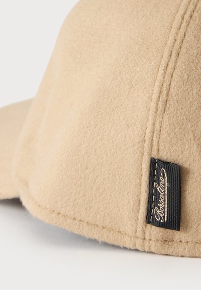 Casquette beige en feutre avec couture visible et petite étiquette en tissu noire rectangulaire cousue près du bord.