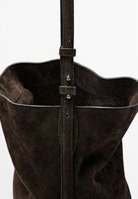 Brun ruskind tote taske med en blød tekstur, bred åbning og justerbar skulderrem med metalhardware og synlige sømdetaljer.