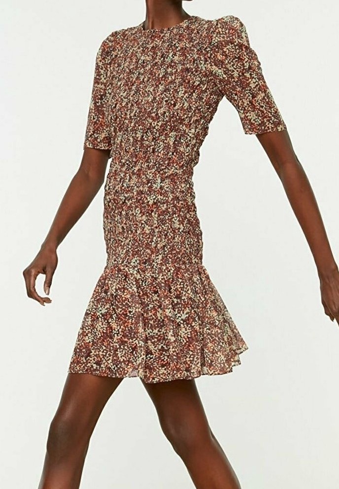 Robe ajustée à manches courtes avec un petit motif floral et un ourlet évasé portée par une personne debout aux bras étendus.