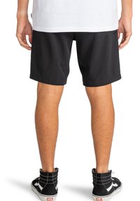Pantalones cortos negros de tejido ligero, con un diseño liso y corte recto. Llevados con zapatillas negras de caña alta.