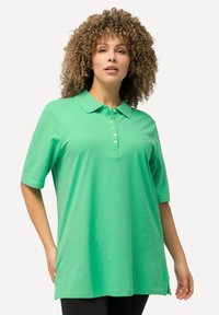 Zelené polo tričko s klasickým límečkem, krátkými rukávy a pěti knoflíky. Vyrobeno z měkkého materiálu s volným střihem a bočními rozparky.