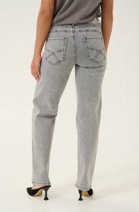 Jeans de mezclilla gris con costuras visibles, dos bolsillos traseros, corte recto, combinados con zapatos de tacón alto negros, tejido texturizado.