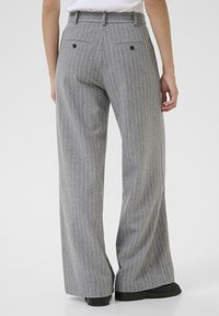 Model wearing gray pinstriped wide-leg trousers from a rear view, showcasing waistband and back pockets. Simple background emphasizes the pants.