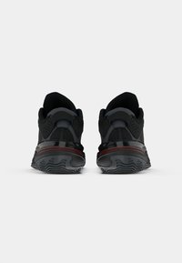 Μαύρα αθλητικά παπούτσια με mesh επάνω μέρος, επενδεδυμένο κολάρο, υφή κάτω μέρος και αντίθεση σε κόκκινες λεπτομέρειες στη μεσόσολα.