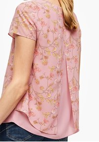 Blusa floreale rosa con maniche corte, caratterizzata da una piega sul retro, realizzata in tessuto leggero. Motivo floreale in toni di rosa e giallo.