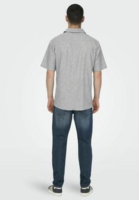 Grijs patroon t-shirt met korte mouwen en een kraag, gecombineerd met blauwe spijkerbroek en zwarte sneakers, gezien van achteren.