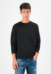 Black sweatshirt with a crew neck, ribbed cuffs, and a tonal logo “REPLAY” on the chest. Paired with distressed blue jeans.