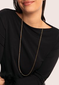 Goldfarbene Kettenohrringe mit bunten Perlen in Orange, Lila und Blau, getragen mit einem schwarzen Oberteil, das eine elegante Drapierung und Textur zeigt.
