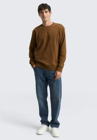 Bruine sweatshirt met ronde hals, gecombineerd met blauwe jeans en witte sneakers. Glad textuur, ontspannen pasvorm en eenvoudig ontwerp.