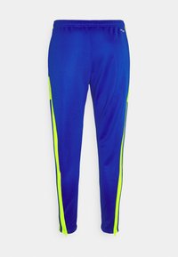 Blå sportbyxor med neon gula sidostreck och dragkedjor vid anklarna, uppvisade mot en enkel vit bakgrund.
