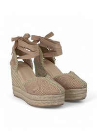 Espadrilles de cuña con textura tejida, color marrón claro y ribete metálico. Presentan cintas largas para atar en el tobillo.