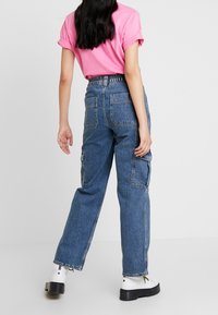 Pantalones cargo de mezclilla azul de talle alto con bolsillos laterales, corte holgado y dobladillos deshilachados, combinados con una camiseta rosa de manga corta.