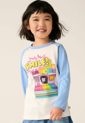 Langarm T-shirt met een witte body en lichtblauwe mouwen, voorzien van een kleurrijke retro camera grafiek en het woord "SMILE!" in vette letters.