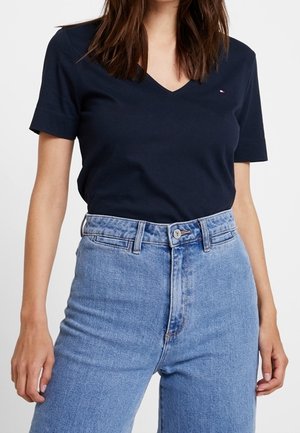 Vrouw die een marineblauw V-hals shirt met korte mouwen draagt, ingestopt in een lichtblauwe, hooggetailleerde spijkerbroek.