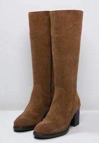 Botas de ante marrón hasta la rodilla con tacón cuadrado y cremallera lateral. Las botas presentan una textura suave y un diseño de punta redondeada.