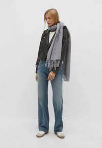 Écharpe grise avec des franges, veste en cuir de motard, top blanc, jeans bleus évasés et baskets blanches. Accent sur les textures et les couleurs.