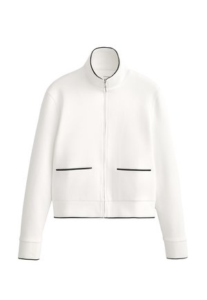 Fehér cipzáras dzseki magas gallérral, fekete díszítéssel és két elülső zsebbel, fekete paszpolozással. Puha, sima anyagból készült.