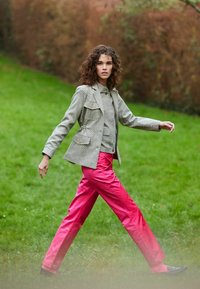Blazer gris à motifs avec deux poches avant, associé à un pantalon rose brillant. Modèle marchant sur l'herbe, portant des chaussures noires.