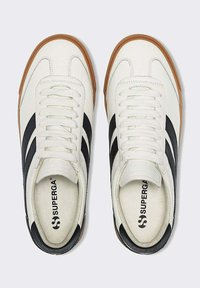 Sneakers bianchi in pelle con strisce nere, suola in gomma, punta tonda e lacci piatti. Presentano il logo "SUPERGA" sulla soletta.