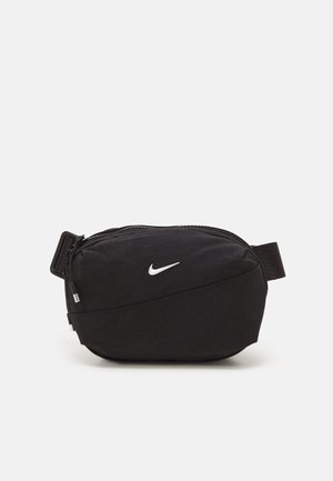 Sac banane Nike noir avec sangle ajustable, poche zippée à l'avant et logo Nike Swoosh blanc sur fond uni.