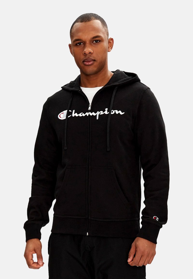 Felpa nera con zip realizzata in tessuto morbido, con cappuccio regolabile tramite un cordino, caratterizzata dal logo bianco "Champion" sul petto e tasche frontali.