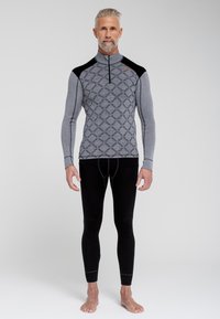Grå langærmet top med et geometrisk mønster og halv lynlås, parret med sorte tætsiddende leggings. Blød tekstur; kontrasterende sorte skulderdetaljer.