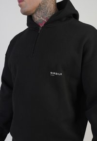 Svart zip-up hoodie i mjukt material, med en logotyp framtill och en avslappnad passform. Strukturerad yta med design av känguruficka.