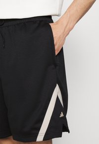Schwarze Sportshorts aus atmungsaktivem Mesh-Material, mit einem seitlichen Akzent in hellem Beige und einem Adidas-Logo nahe dem Saum.