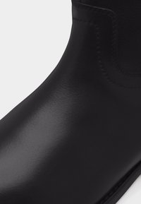 Bottine en cuir noir lisse avec panneau latéral élastique et détails de couture minimalistes.